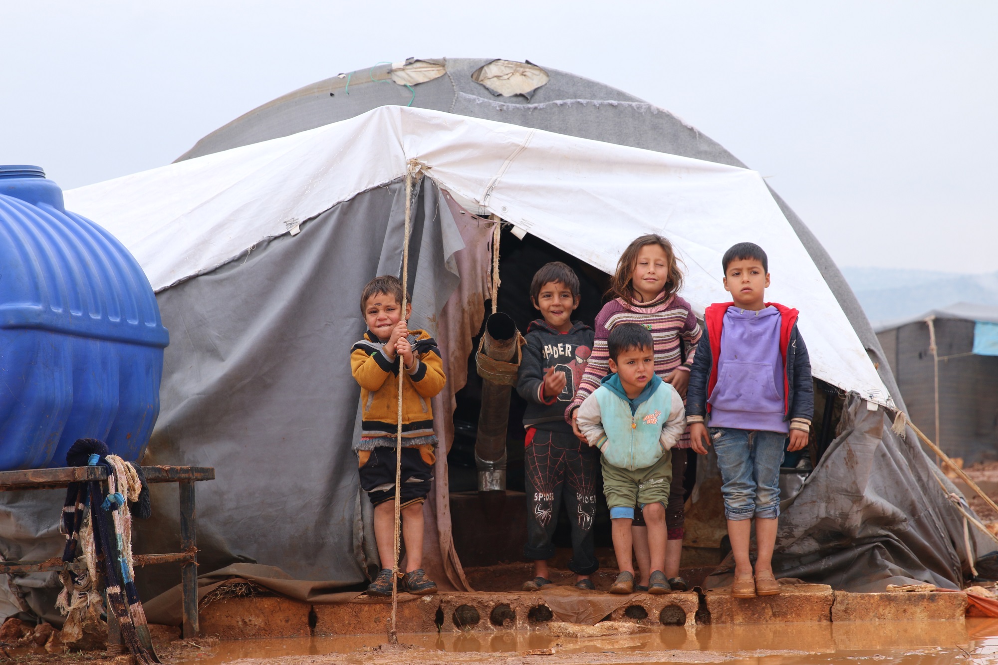 Displaced families in front of a tent in a camp in winter